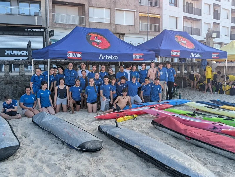 Deportistas do club xunto ás táboas e surf skis baixo as carpas de Salvamento Arteixo